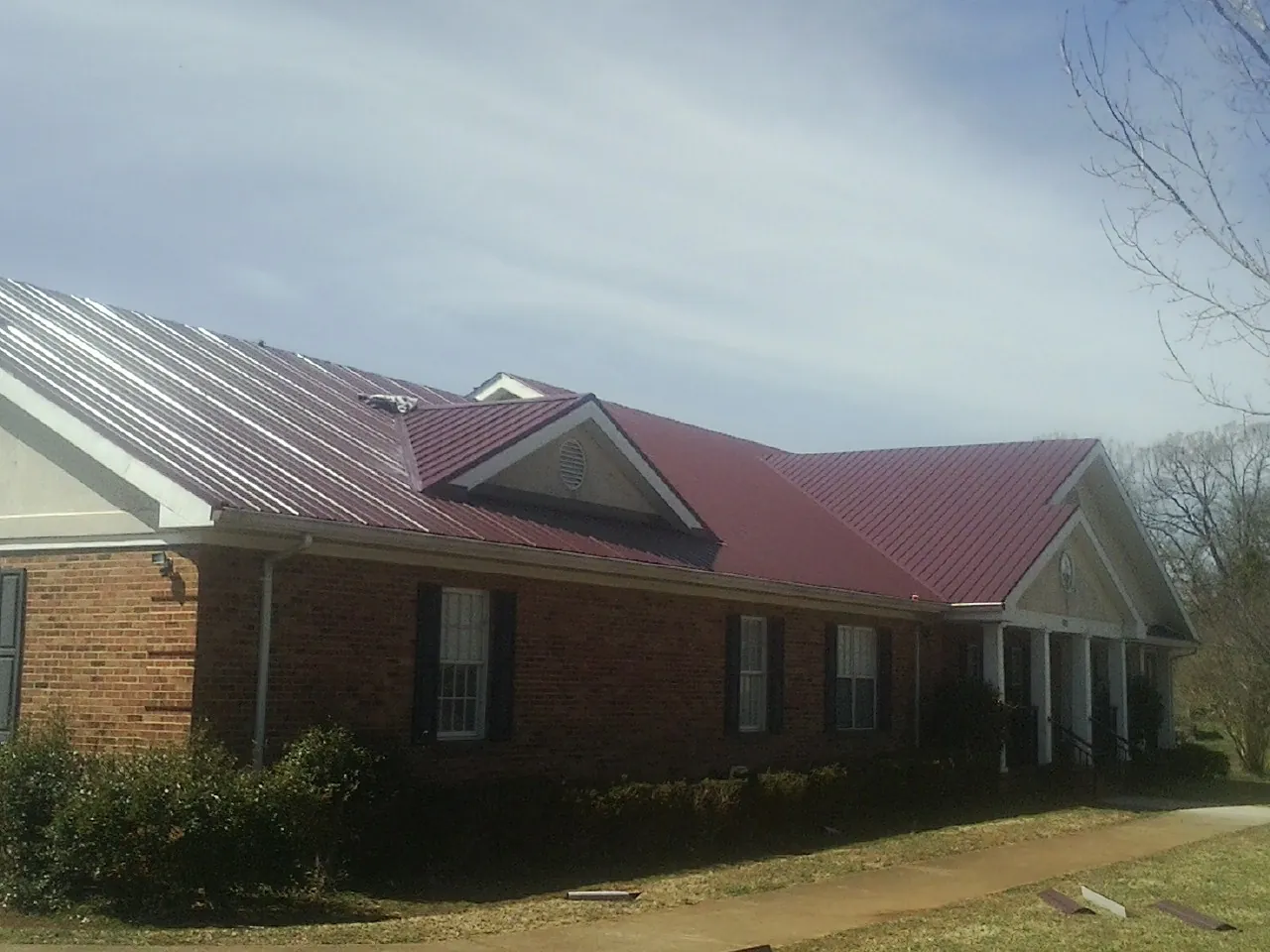 Red metal roof with gabled entries on a long brick building, from a Hail Damage Roof Repair job in Westmoreland
