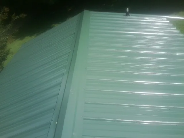 New green metal panels meeting at the ridge of a roof — Flat Roof Repair work by our crew in Westmoreland
