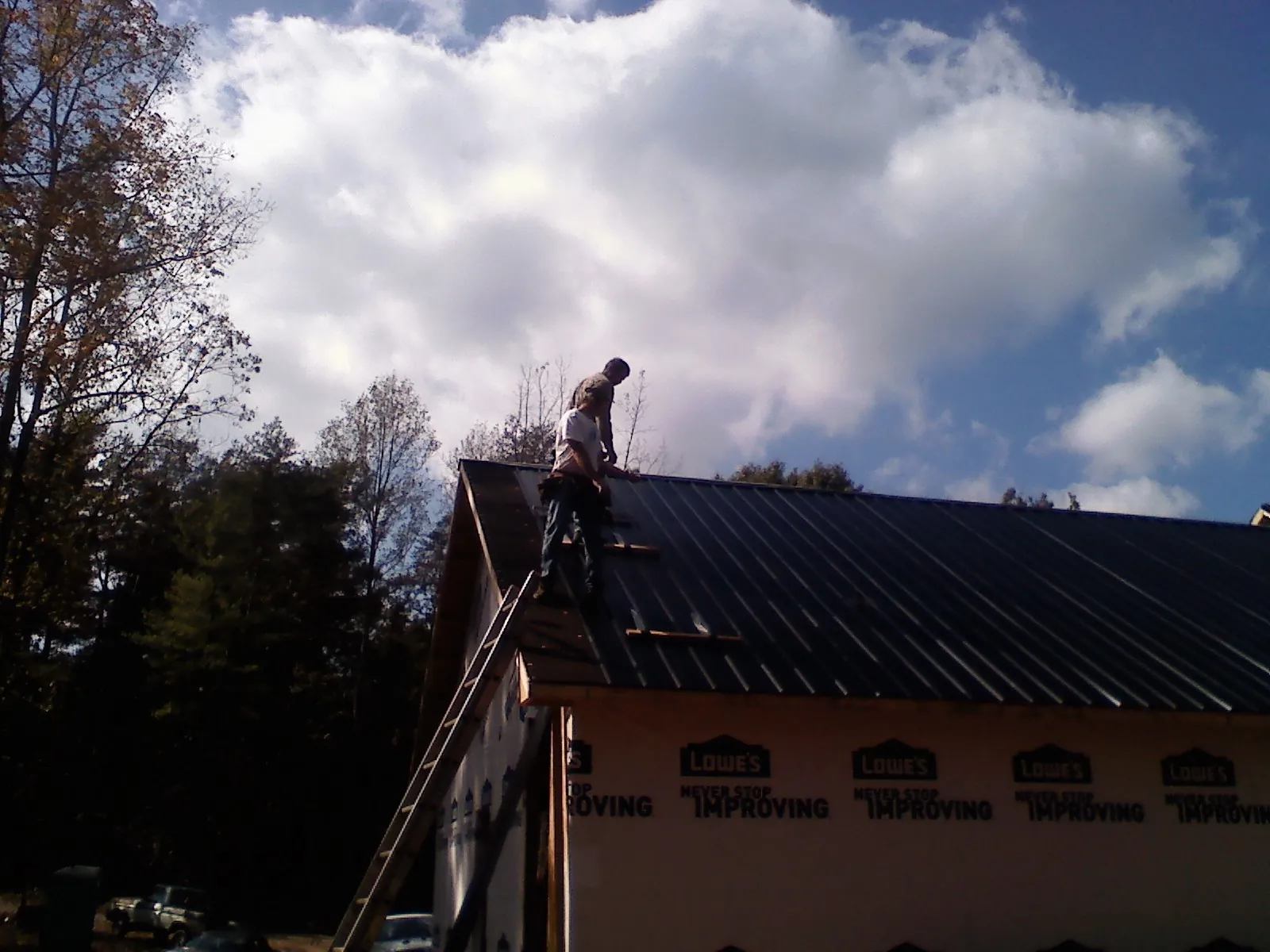 Roofer fastening dark metal panels high against a cloudy sky, from a Roof Inspection job in Westmoreland